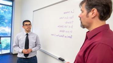 student and professor talking in front of white board with Spanish phrases